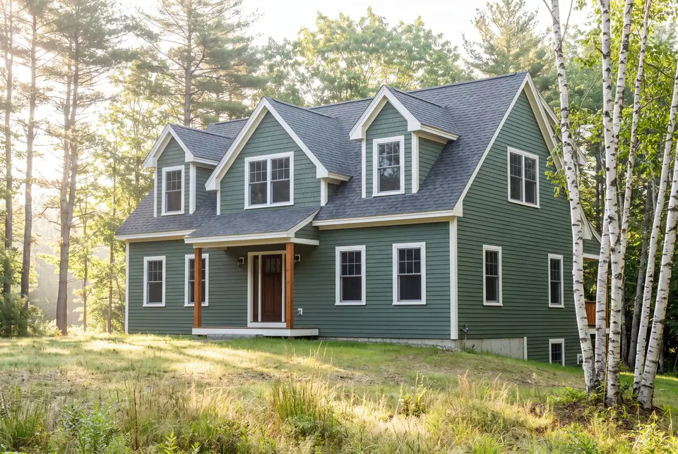 Illustration: A newly built two-story green house with a dark roof and white trim, surrounded by grass and trees under a bright sky