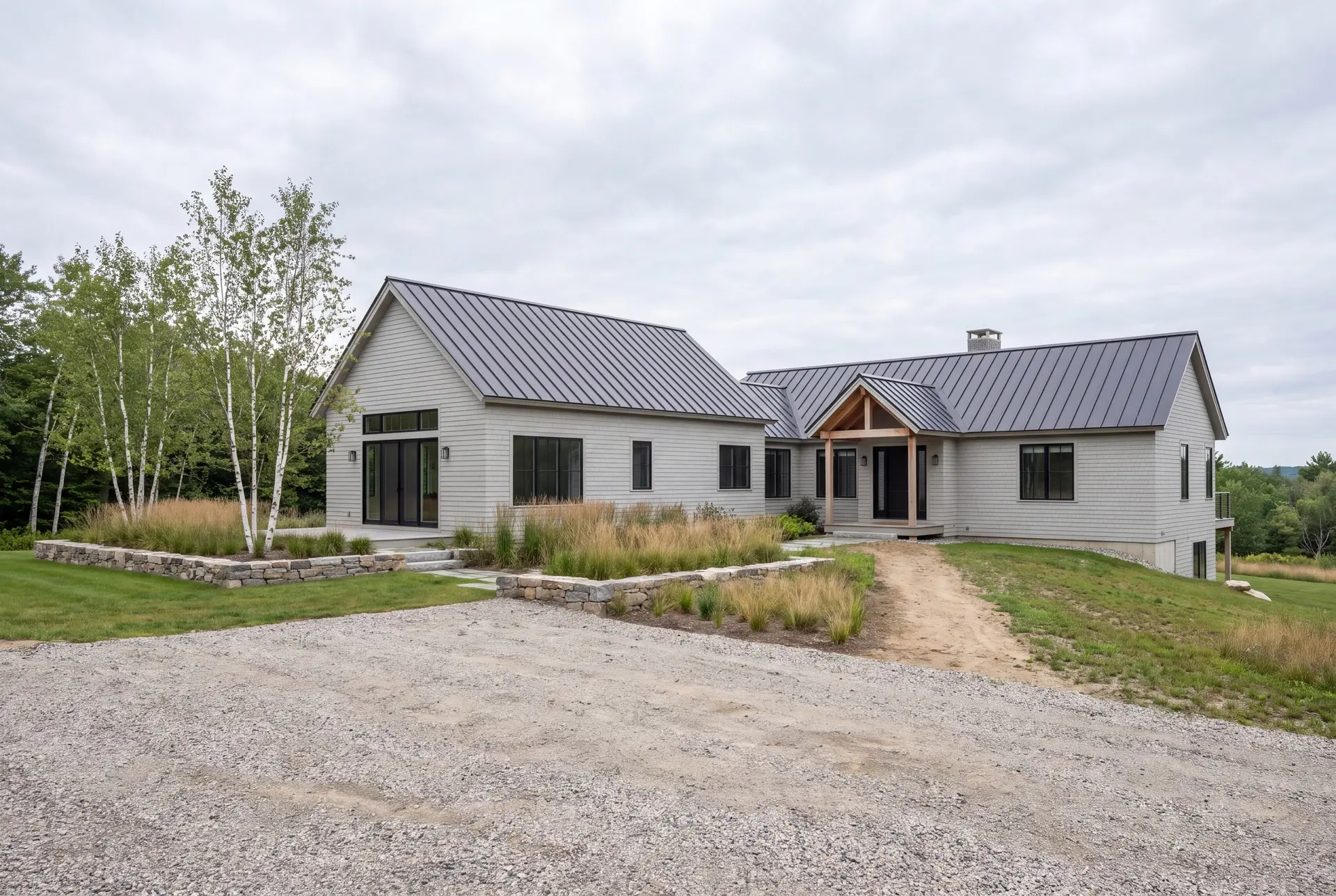 Illustration: A modern single-story house with light gray siding and a dark metal roof, set against a natural landscape with trees and a cloudy sky