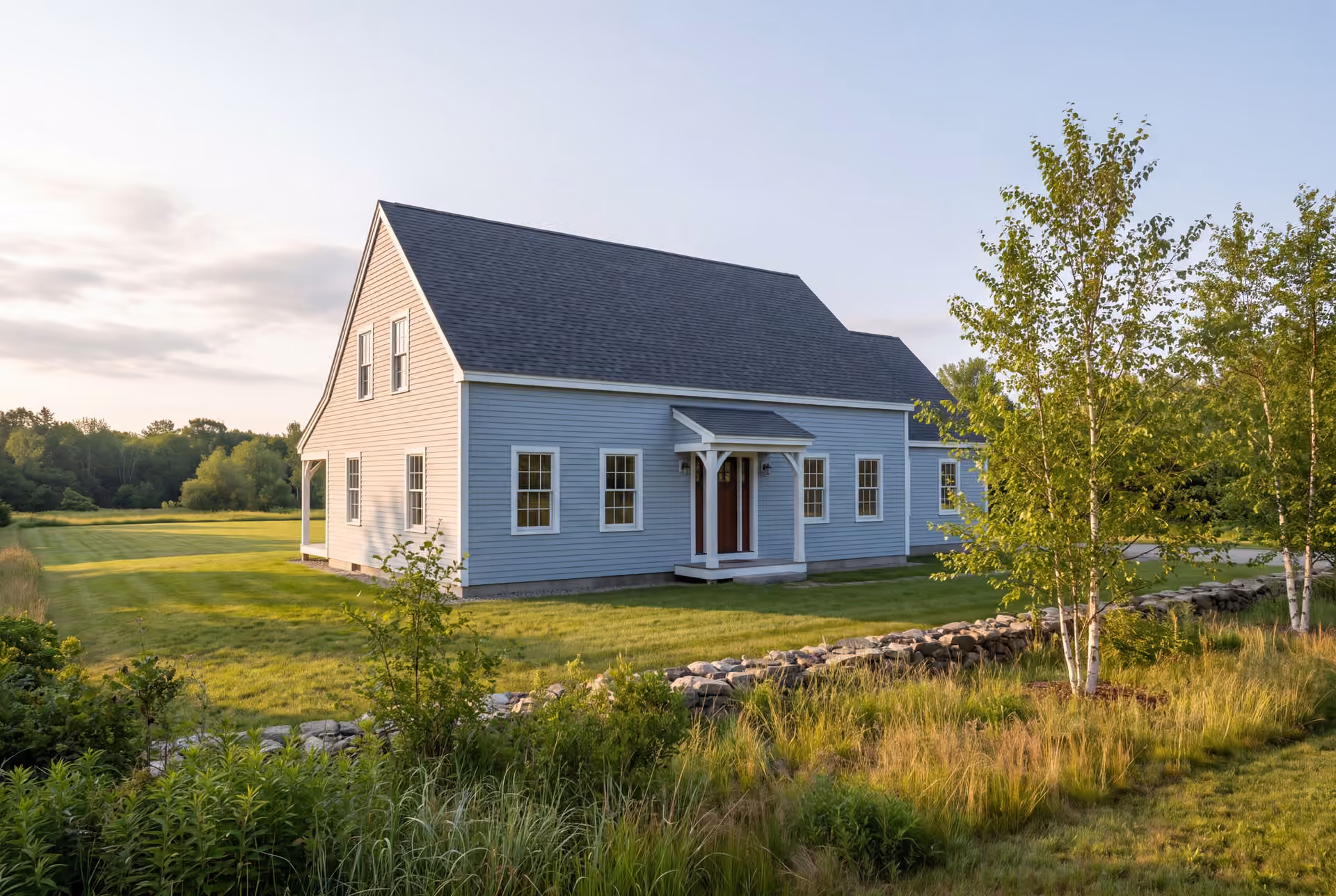 general contractor in Old Orchard Beach, ME: illustrative scene, A light blue saltbox house with a dark roof and white trim, surrounded by green grass and trees under a clear sky