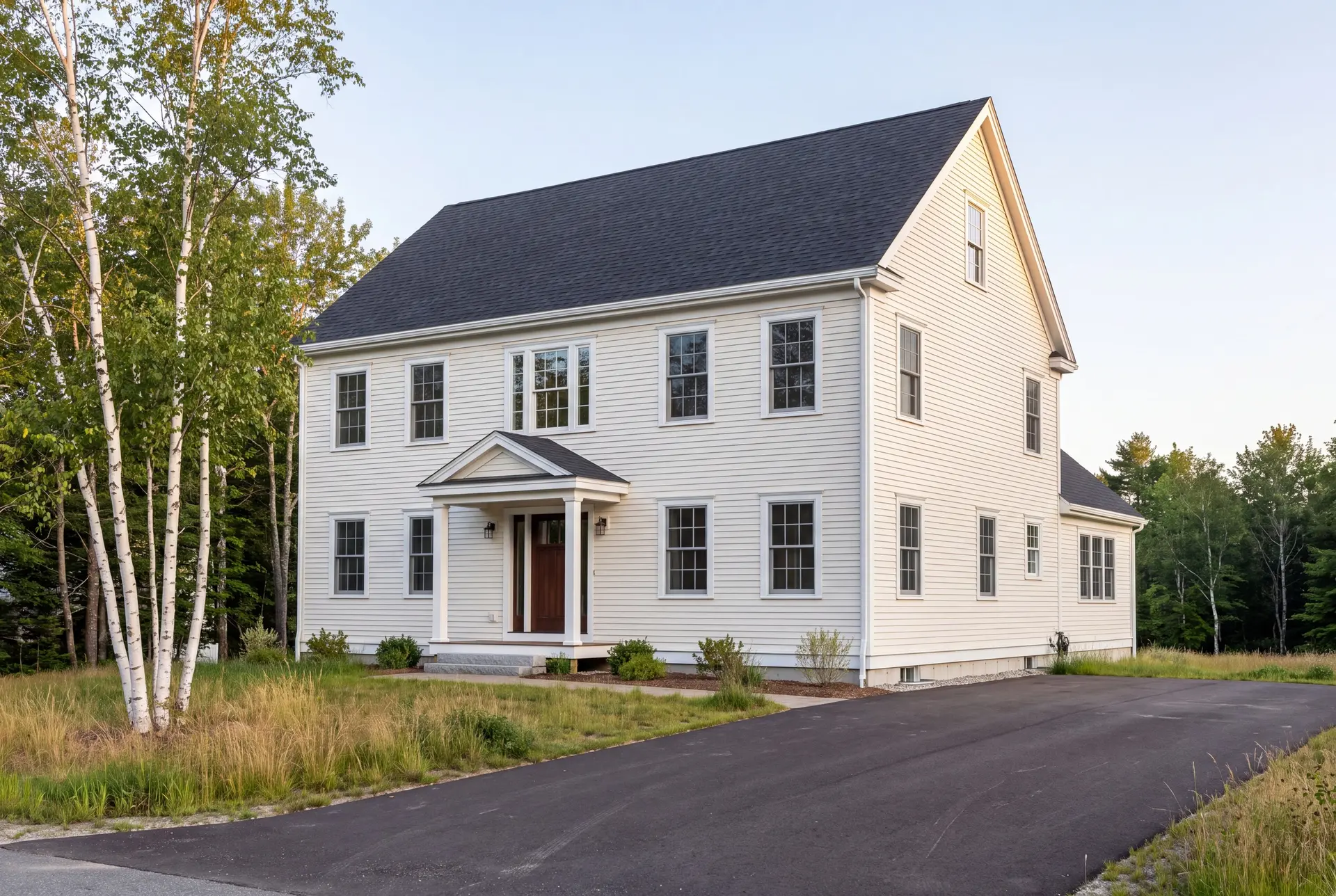 Illustration: A newly built two-story white Colonial house with a dark roof, a covered front entry, and a paved driveway, set against a backdrop of trees and grass