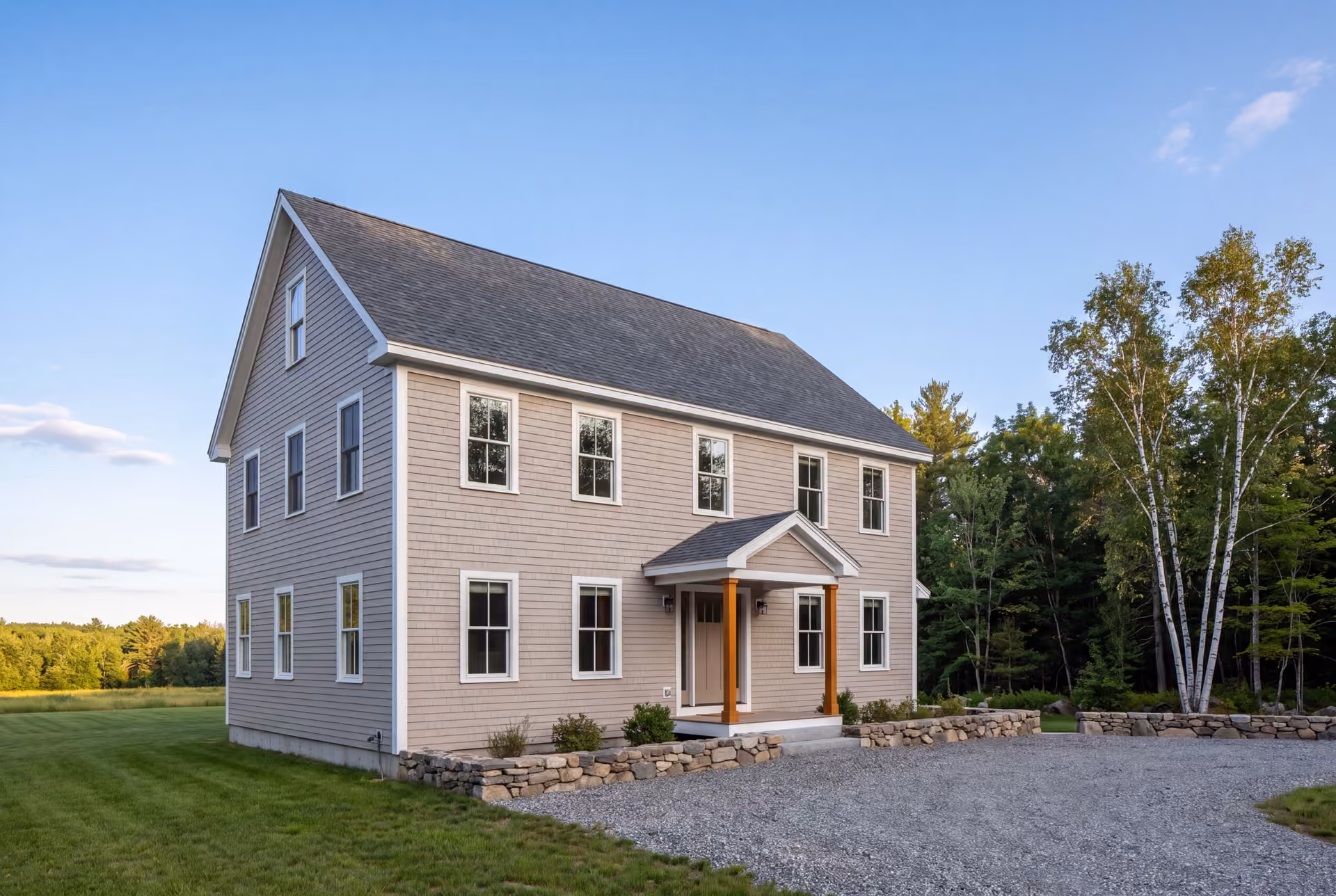general contractor in Sanford, ME: illustrative scene, A newly built two-story shingle-style house with light siding, a dark roof, and white-trimmed windows, viewed from a three-quarter angle with a gravel driveway and trees