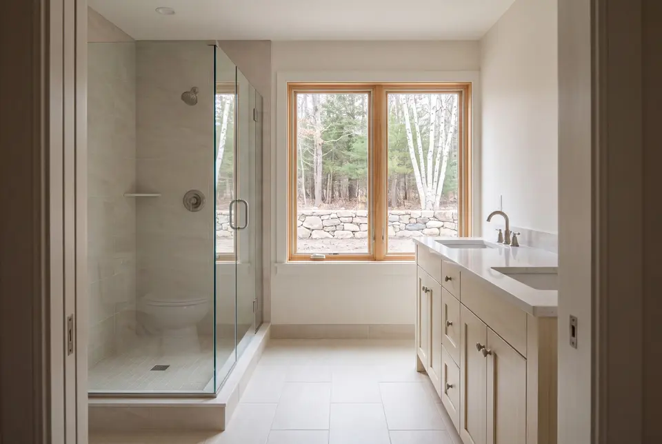 Illustration: A bright, clean bathroom with a double vanity, a glass shower, and a large window overlooking a natural landscape