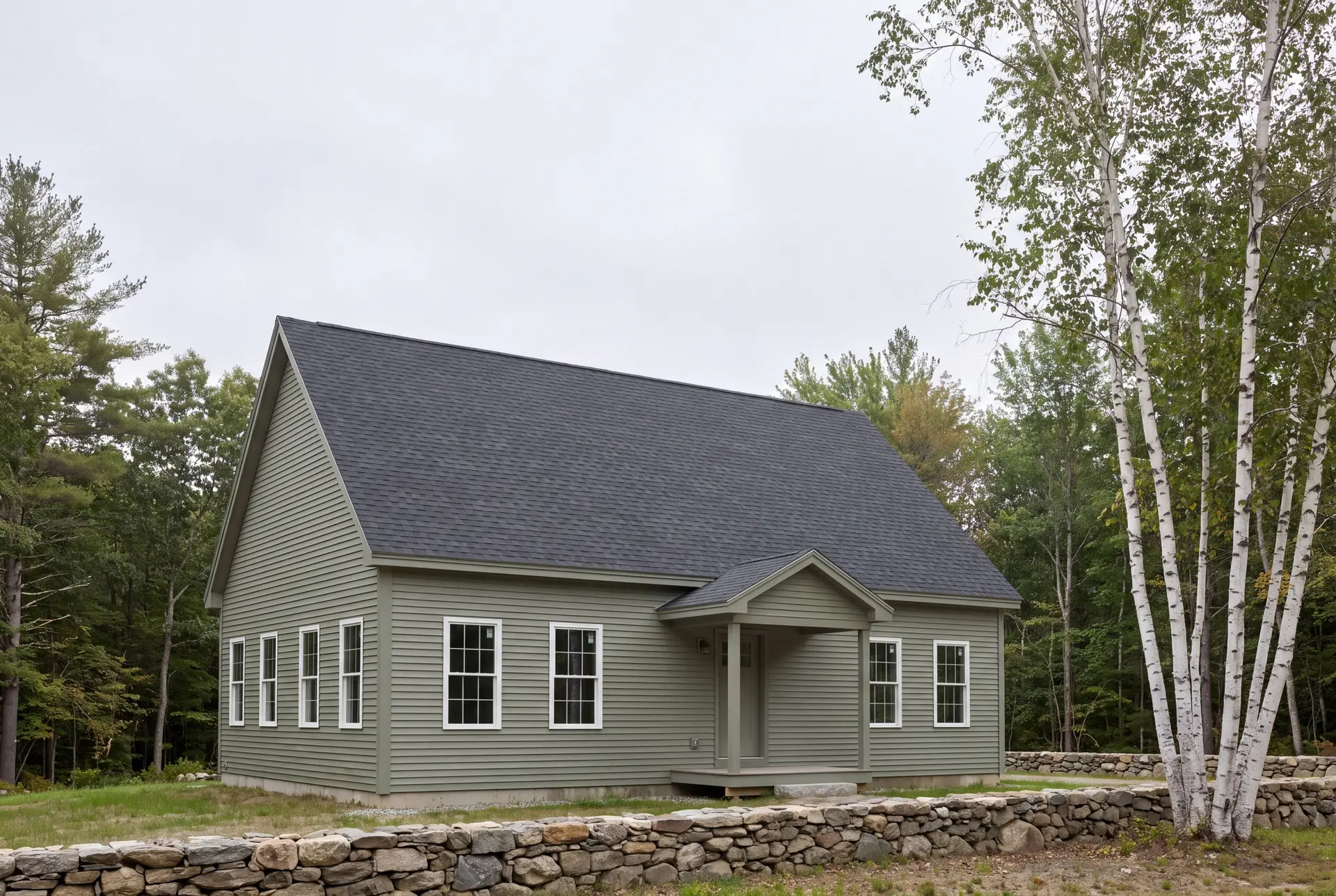 Illustration: A sage green gabled house with a dark gray roof, white-trimmed windows, and a covered entry, set against a backdrop of trees and a stone wall