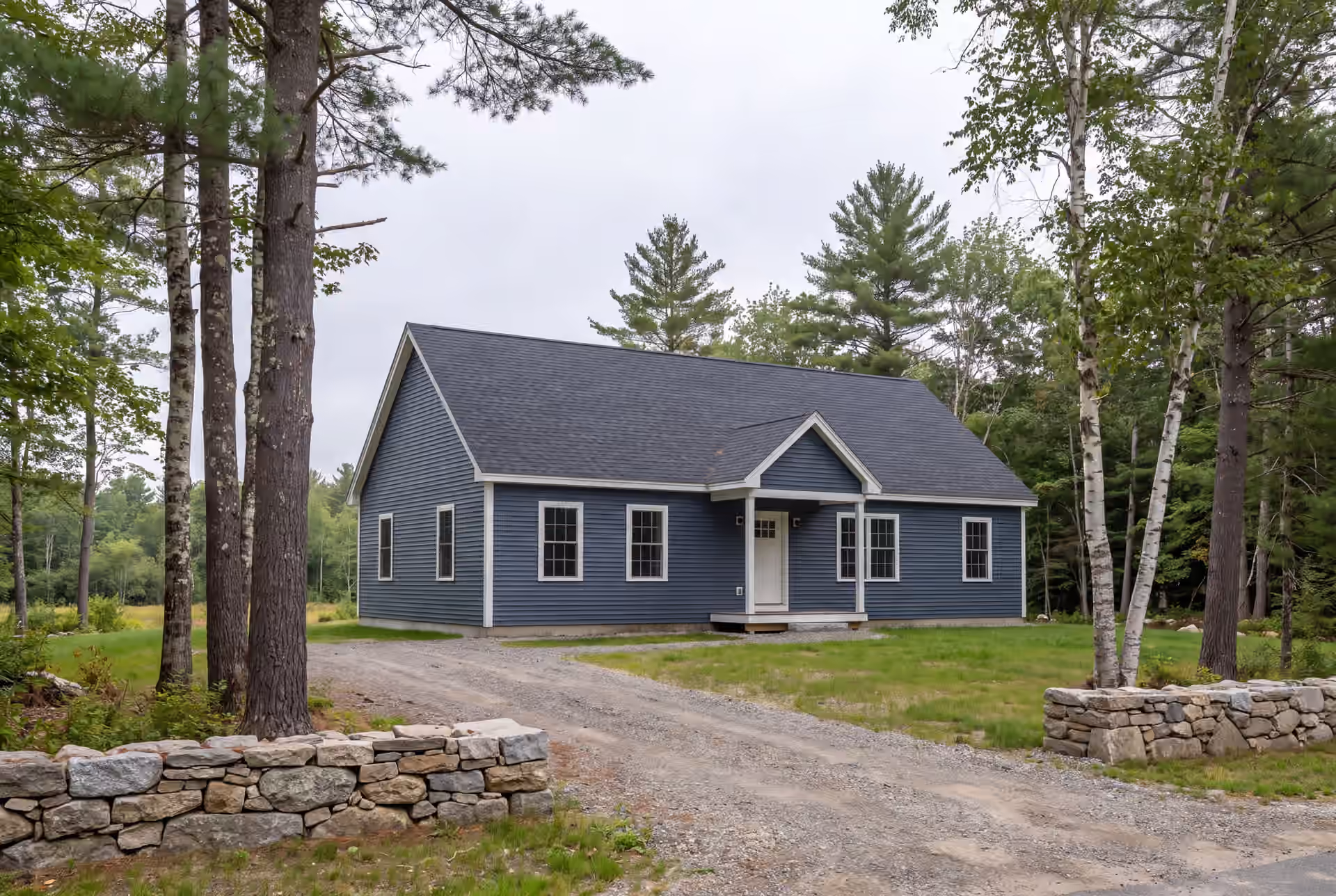 Legacy Construction: illustrative scene, A newly built blue ranch house with a dark roof and white trim, surrounded by trees and a gravel driveway