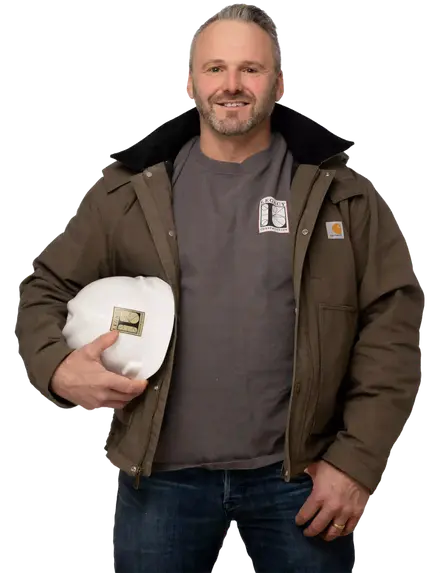Joe Hausler wearing a brown jacket and holding a white Legacy Construction hard hat