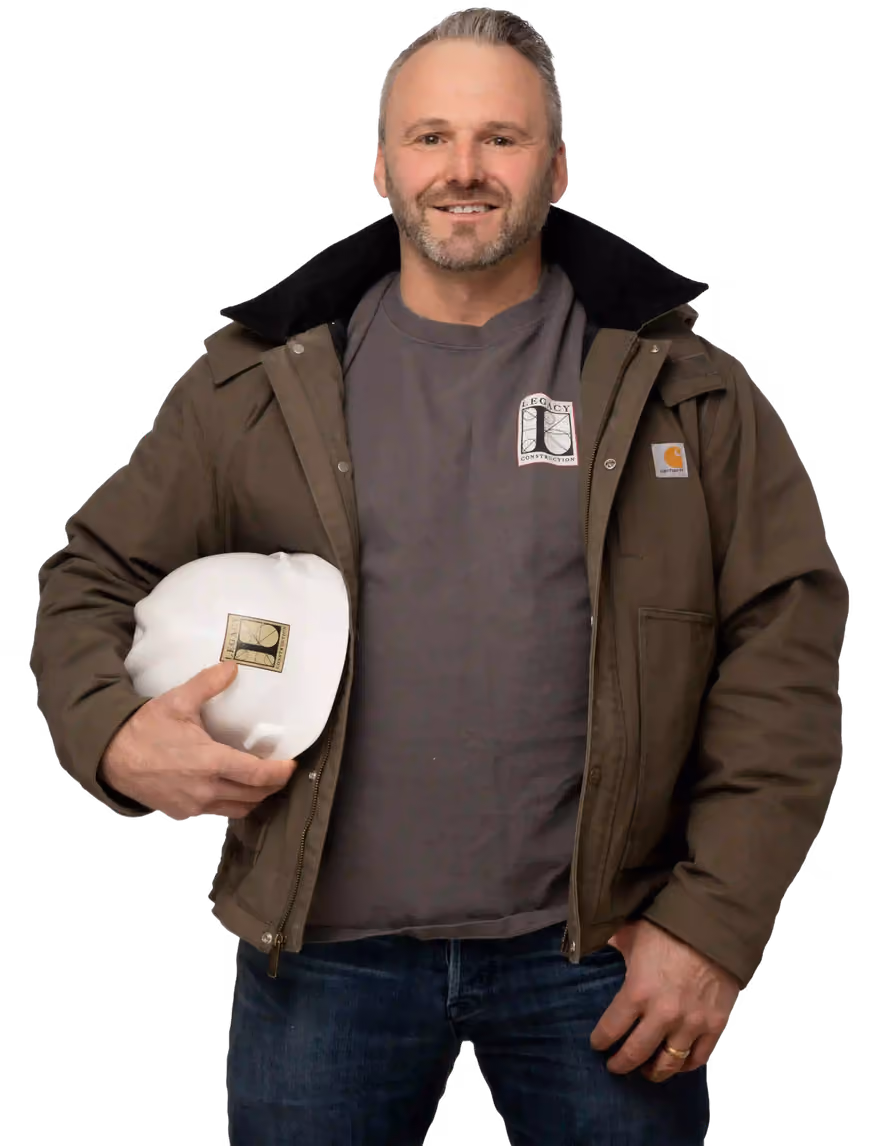 Joe Hausler wearing a brown jacket and holding a white Legacy Construction hard hat